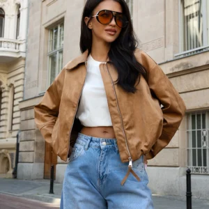 Rozpięta modna kurtka damska zestawiona z klasycznym topem i spodniami z denimu.